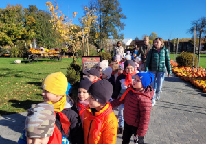 Dzieci spacerują alejkami i obserwują jesienne dekoracje
