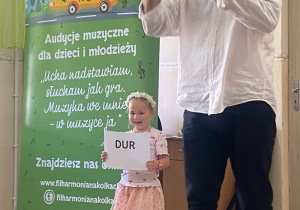 Radosna dziewczynka pokazuje napis, którego znaczenie tłumaczy pan Maciej.