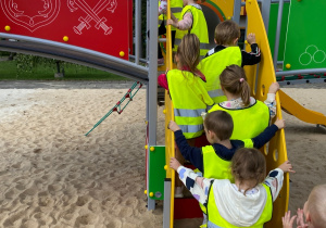 Dzieci jedno za drugim wchodzą po drewnianych schodkach, będących częścią konstrukcji placu zabaw.