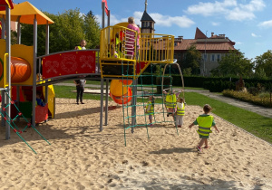 Dzieci biegają po piasku wokół urządzeń do zabawy.