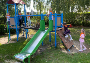 Dziewczynka wspina się na ściankę, dwoje dzieci przechodzi po równoważni, jeden chłopiec zjeżdża na drążku.