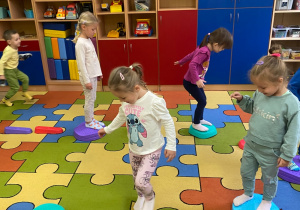 Dziewczynki i chłopcy przechodzą po kolorowych, podłużnych i okrągłych kamieniach sensorycznych.