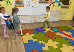 Chłopiec idzie po kamieniach sensorycznych w kierunku dziewczynki, która wręcza mu prezent.