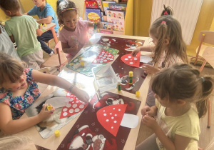 Dziewczynki ozdabiają papierowe muchomorki kropkami