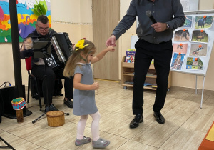 Pan Maciej wraz z dziewczynką tańczy w takt granego utworu, dziewczynka trzyma w dłoni żółty kwiat.