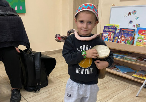 Chłopiec wygrywa dźwięki na marokańskim bębenku, na głowie ma kolorową, marokańską czapeczkę a szyję oplata mu "wąż".