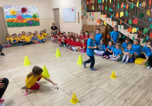 Chłopiec w niebieskiej koszulce i dziewczynka w żółtej koszulce biegną slalomem, trzymając trzymając łyżeczkę na której jest kasztan.
