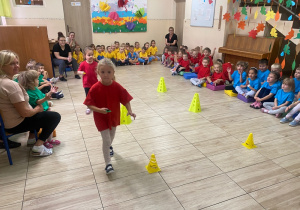 Dziewczynki w czerwonych koszulkach przenoszą na łyżeczce kasztana.