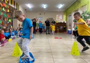 Chłopcy w żółtej i niebieskiej koszulce biegnąc omojają żółte pachołki.