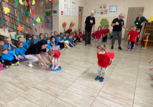 Przedszkolaki w czerwonych koszulkach przekładają przez siebie szarfy.