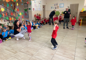 Przedszkolaki w czerwonych koszulkach przekładają przez siebie szarfy.