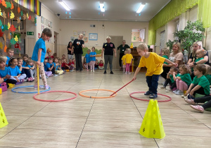 Chłopiec w żółtej koszulce i dziewczynka w niebieskiej koszulce przesuwają za pomocą kijka obręcze.