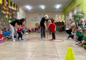 Chłopcy w czerwonych koszulkach przesuwają za pomocą kijka obręcze.