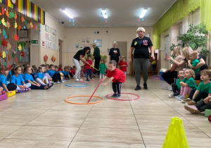 Chłopcy w czerwonych koszulkach przesuwają za pomocą kijka obręcze.