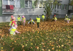 Dzieci w kamizelkach odblaskowych podrzucają do góry jesienne liście
