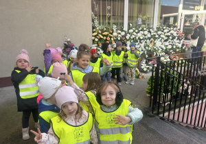 Dzieci w kamizelkach odblaskowych z wizytą w kwiaciarni