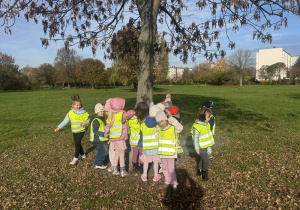 Dzieci w kamizelkach odblaskowych przytulają się do drzewa