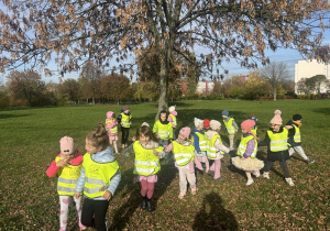 Dzieci w kamizelkach odblaskowych przytulają się do drzewa
