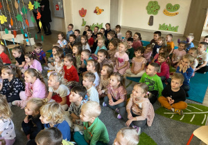 Uśmiechnięte dzieci siedzą na dywanie i czekają na rozpoczęcie przedstawienia.