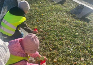 Dzieci stawiają znicze na grobie