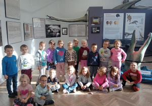 Grupa dzieci pozuje do zdjęcia na tle wystawy.