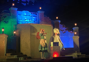 Główna bohaterka i "Gęś" na tle scenografii - fragment miasta.