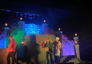 Chłopiec, policjant i kucharz na tle scenografii - fragment miasta.