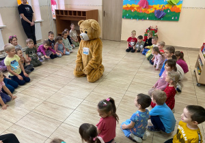 Dzieci siedzą w kole, wewnątrz którego siedzi miś Tedi.