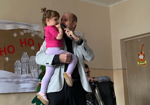 Pan Maciej trzyma na rękach dziewczynkę i śpiewa kolędę.