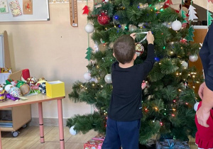 Chłopiec wiesza swoją bombkę na choince
