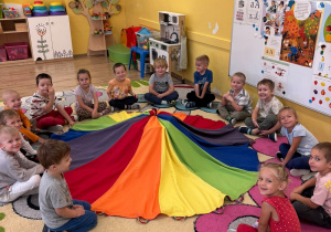 Dzieci siedzą w kole i oczekują na niespodziankę ukrytą pod chustą animacyjną.
