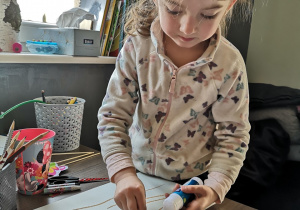 Dziewczynka przykleja kulki waty na narysowane gałązki