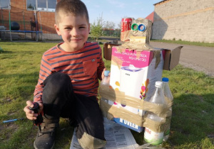 Chłopiec prezentuje skonstruowanego z kartonów i butelek robota