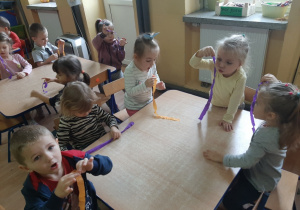Dzieci przy stolikach dmuchają na pasek bibuły