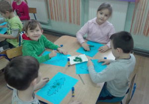 Dzieci wypełniają brokatem narysowane choinki