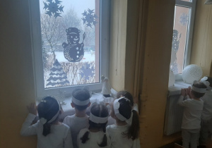 Dzieci spoglądają przez okno na zimowy ogród