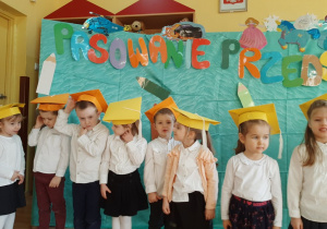 Dzieci stoją ubrane w żółte czapeczki.