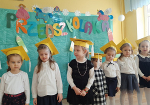 Dzieci stoją ubrane w żółte czapeczki.
