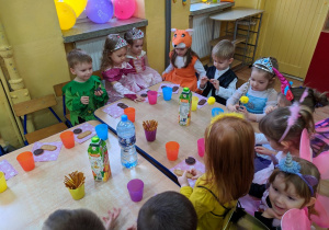Dzieci siedzą przy stoliku i jedzą słodki poczęstunek.