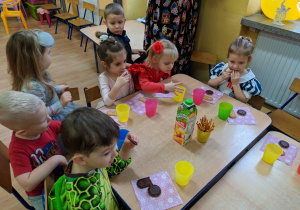 Grupa dzieci siedzi przy stoliku i je słodki poczęstunek.