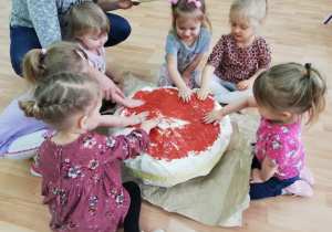 Dzieci malują wykonanego pączka dłońmi umoczonymi w brązowej farbie.