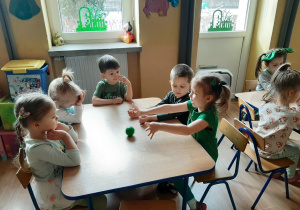 Dzieci siedzą przy stolikach, turlają do siebie zieloną, małą piłkę i mówią - „Co jest zielone?”.
