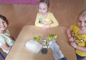 Trzy dziewczynki siedzą przy stoliku, na którym zgromadzone są materiały do wykonania zajączka.