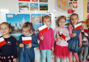 Dziewczynki prezentują Symbole Narodowe i słuchają wiersza „Katechizm polskiego dziecka”.