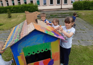 Dwie dziewczynki i chłopiec dokańczają malować domek