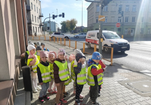 Dzieci stoją w pobliżu sygnalizacji świetlnej i obserwują ruch uliczny.