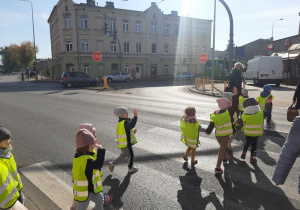Przedszkolaki przechodzą po pasach na skrzyżowaniu ulic.