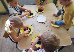 Dzieci wysypują ziarenkami środek papierowego słonecznika