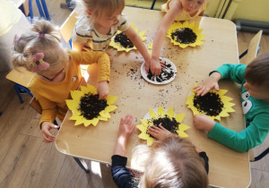 Dzieci wysypują ziarenkami środek papierowego słonecznika