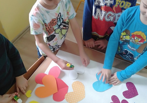 Dzieci wspólnie układają na kartonie bukiet z serc